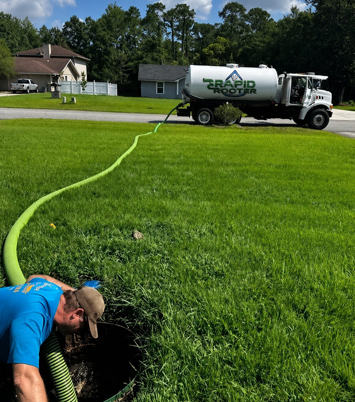 Rapid Rooter vacuum truck pumping a septic tank from the street, hose run across the lawn